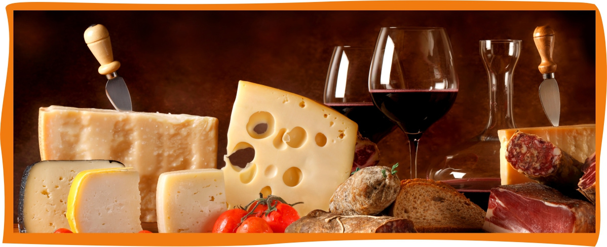 Das Bild zeigt eine Auswahl verschiedener Käsesorten, Brot und Wurst, ergänzt durch zwei Gläser Rotwein. Es vermittelt ein elegantes, kulinarisches Thema mit mediterranem Flair.