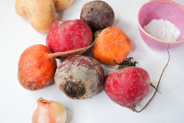 KI generiert: Rote Bete, Kartoffeln und eine Zwiebel liegen neben einer Schale mit weißem Pulver auf weißem Hintergrund.