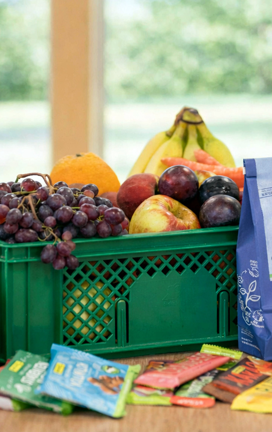KI generiert: Eine grüne Kiste mit frischem Obst und verschiedenen Snacks auf einem Tisch.