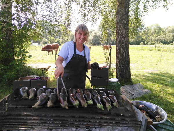KI generiert: Eine Person grillt Auberginen in einem grünen, ländlichen Umfeld.