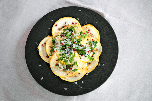 KI generiert: Ein Teller mit dünn geschnittenem Gemüse, Kräutern und geriebenem Käse auf schwarzem Untergrund.