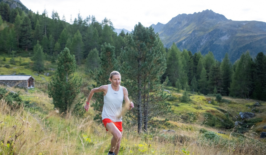 KI generiert: Ein Mensch joggt durch eine bergige Landschaft mit Bäumen und Hügeln.