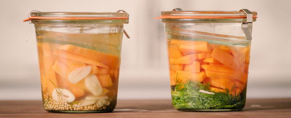 KI generiert: Zwei Gläser mit eingelegtem Gemüse und Kräutern auf einem Tisch.
