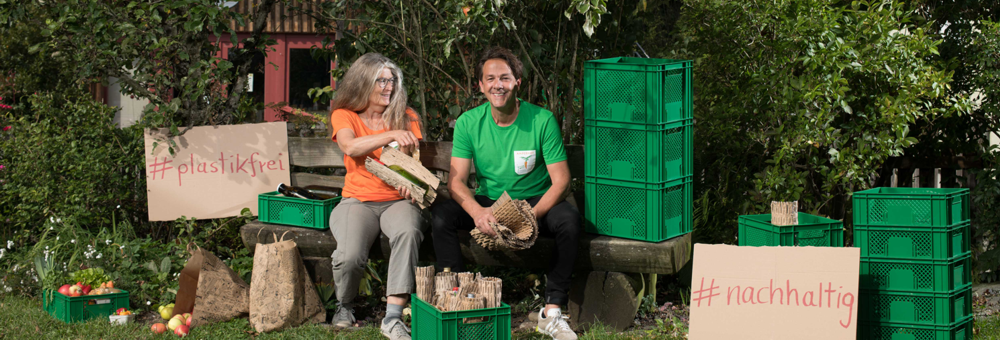 Gründerin Gisela Kinzelmann und Geschäftsführer Ullrich Vogt-Bergener sitzen unter einmem Apfelbaum umgeben von Ökokisten.