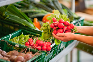 KI generiert: Frischer Marktstand mit Radieschen und anderem Gemüse in grünen Kisten. Hände halten Radieschen.