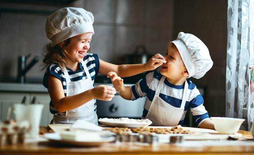 Zwei Kinder feixen und naschen in der Weihnachtsbäckerei