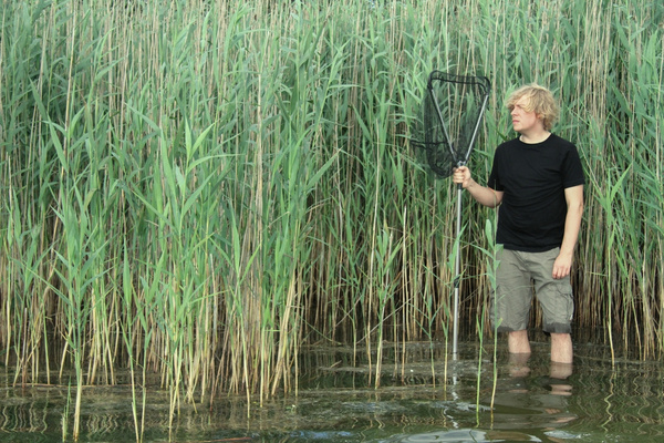 KI generiert: Eine Person steht im Wasser und hält ein Netz, umgeben von hohem Schilf.
