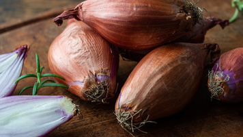 KI generiert: Frische Schalotten liegen auf einem Holztisch, zwei sind aufgeschnitten.