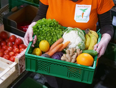 Eine Person hält eine mit buntem Obst und Gemüse gefüllte Ökokiste.