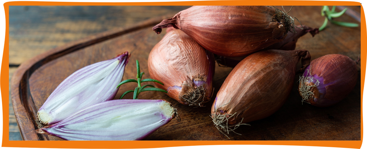 KI generiert: Schalotten auf einem Holzbrett, einige ganz, eine halbiert. Keine zusätzlichen Texte.