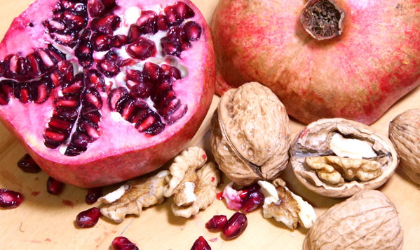KI generiert: Das Bild zeigt einen aufgeschnittenen Granatapfel, dessen dunkelrote Kerne sichtbar sind, zusammen mit Walnüssen auf einem Tisch. Der Hauptfokus liegt auf den frischen Früchten und Nüssen.