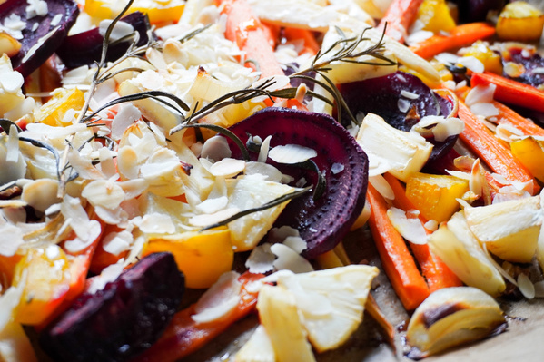 KI generiert: Das Bild zeigt eine bunte Mischung aus geröstetem Gemüse wie Karotten, Rote Bete und Paprika, bestreut mit Mandelsplittern und garniert mit Rosmarinzweigen. Die Präsentation ist rustikal und appetitlich.