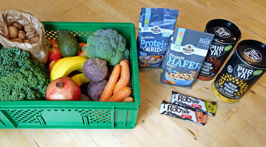 KI generiert: Eine grüne Kiste voller Obst und Gemüse neben Proteinprodukten auf einem Tisch.