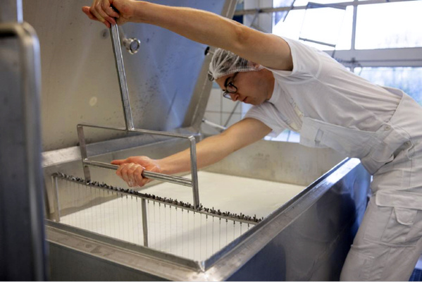 KI generiert: Eine Person in weißer Kleidung rührt mit einem Metallgerät in einem großen Gefäß mit Flüssigkeit.