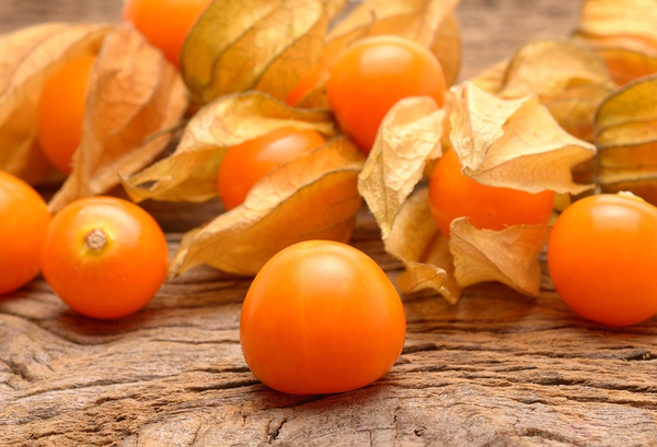 KI generiert: Orangenfarbene Physalis mit getrockneten Blättern liegen auf einer rustikalen Holzoberfläche.