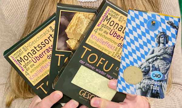 KI generiert: Person hält vier Tofu-Packungen, darunter Monats- und Weißwurst-Tofu.