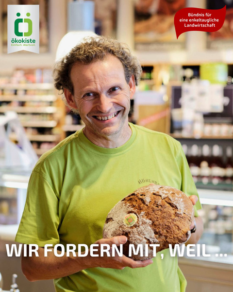 KI generiert: Ein Mann in einem Geschäft hält ein Brot. Text: "WIR FORDERN MIT, WEIL …"