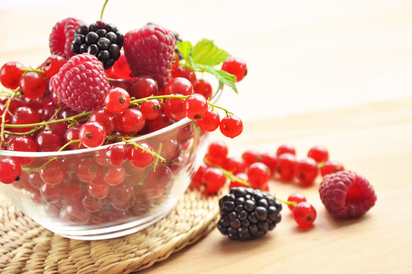 KI generiert: Eine Schale mit Himbeeren, Brombeeren und roten Johannisbeeren auf einem Holztisch.
