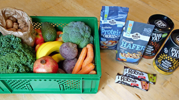 KI generiert: Das Bild zeigt eine Auswahl an frischem Wurzelgemüse, darunter Karotten, Rote Bete, Sellerie, Pastinaken und Kartoffeln sowie eine Packung Mandelblättchen. Die Zutaten liegen auf einer grauen Oberfläche und sind größtenteils in einem geflochtenen Korb arrangiert.