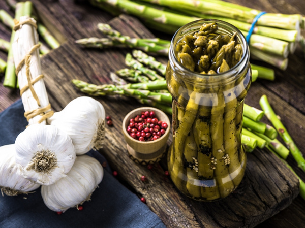 KI generiert: Ein Glas eingelegter Spargel, daneben Knoblauch, roter Pfeffer und frischer Spargel.