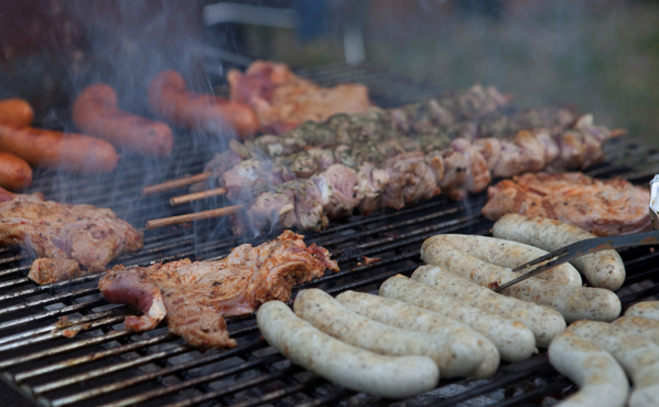 KI generiert: Verschiedene Fleischsorten wie Würstchen und Spieße werden auf einem Grill zubereitet.
