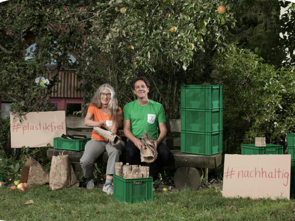 KI generiert: Zwei Personen sitzen im Garten mit Obstkisten, Schildern "#plastikfrei" und "#nachhaltig".