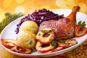 KI generiert: Das Bild zeigt ein festliches Gericht mit Rotkraut, zwei Knödeln und einem Entenbraten, garniert mit gebratenen Apfelscheiben. Es ist dekorativ angerichtet und vermittelt eine warme, einladende Atmosphäre.
